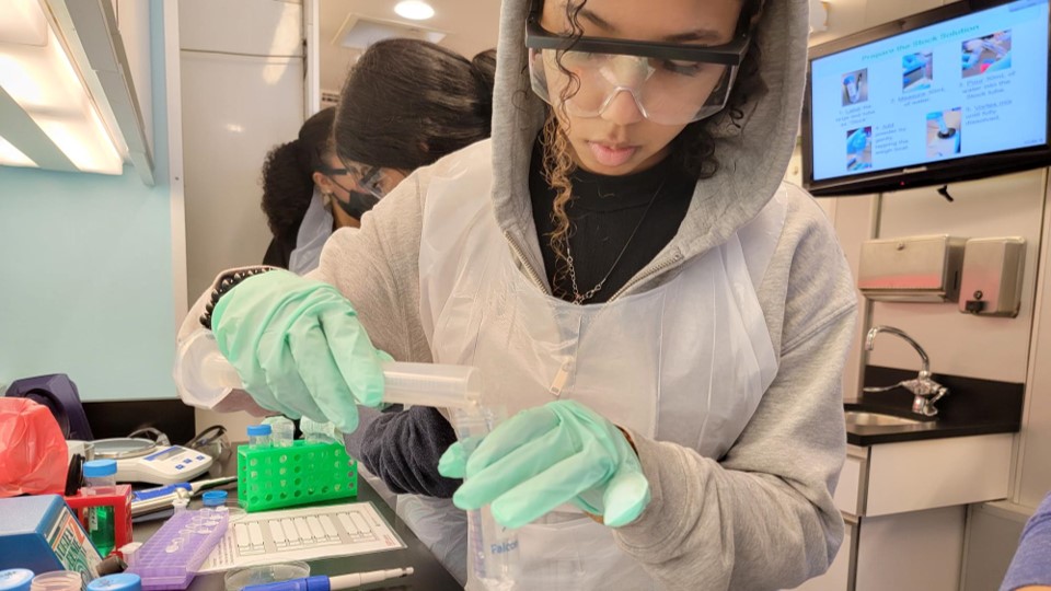 A student uses a graduated cylinder to measure chemicals for a colorimetric assay onboard Seattle Children's Research Institute's mobile Science Adventure Lab.